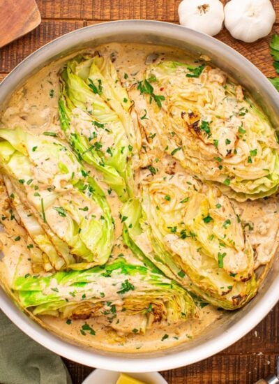 Creamy Garlic Parmesan Cabbage in a skillet on table with parlsey and garlic beside it on table