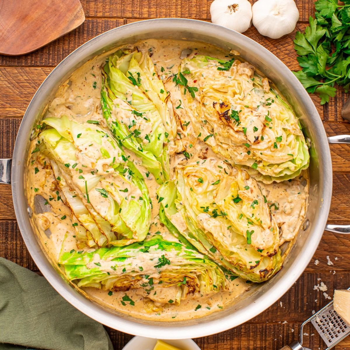 Creamy Garlic Parmesan Cabbage in a skillet on table with parlsey and garlic beside it on table 