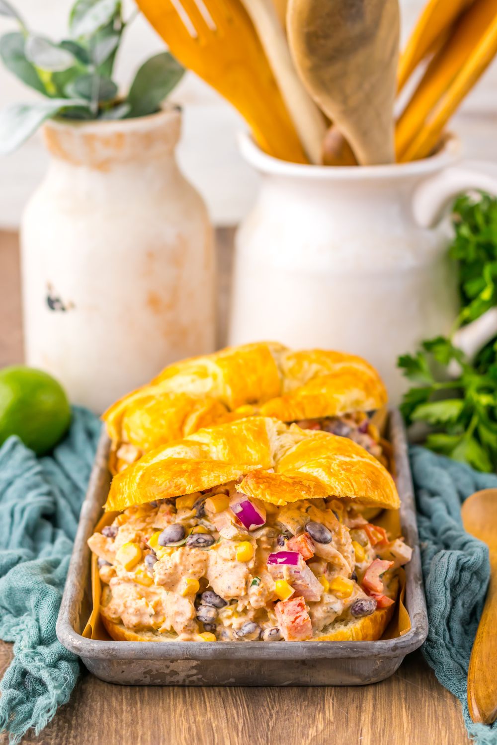 Creamy Taco Chicken Salad on croissants on table in tray with wooden spoons behind it on table 