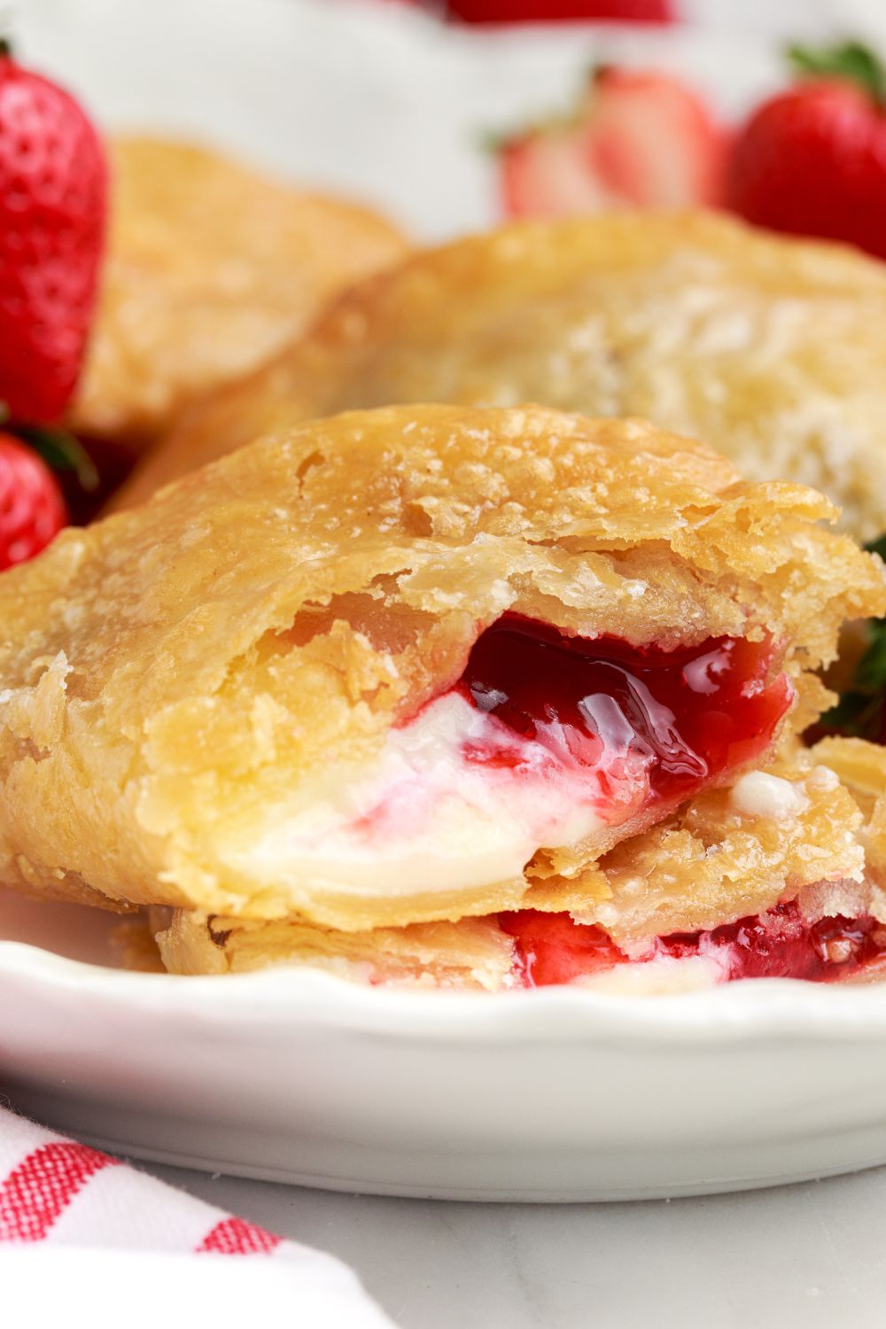 Deep Fried Strawberry Cheesecake Pie on table with strawberries and a red and white towel to side 