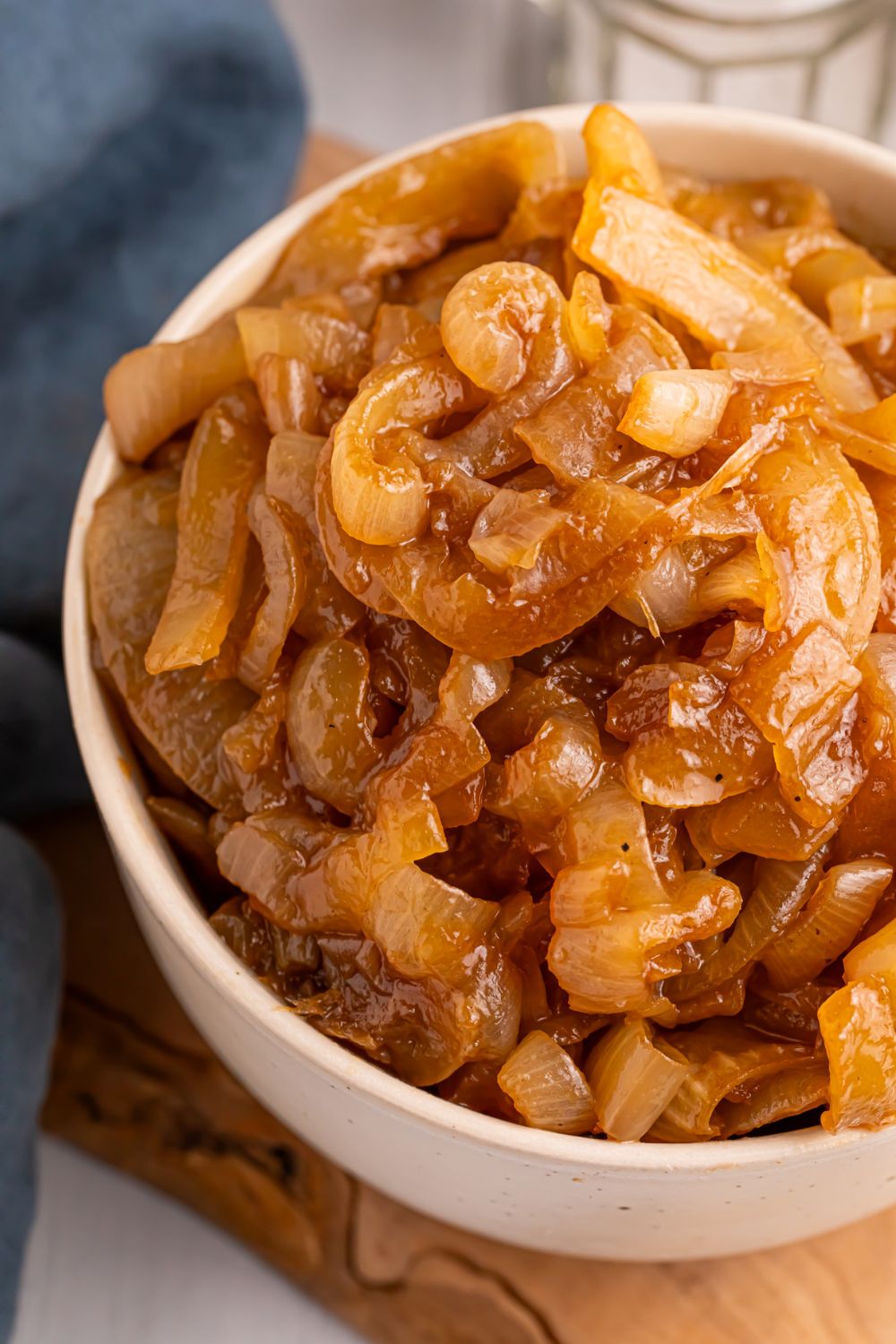 CrockPot Caramelized Onions in a white bowl on table with a blue towel to side of it 