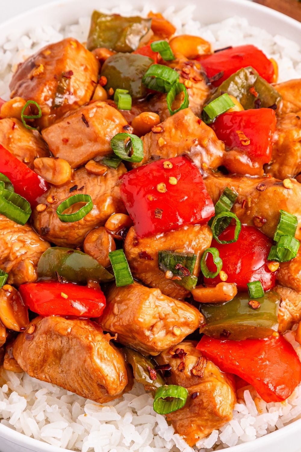 Better Than Takeout Kung Pao Chicken on a plate with rice under it with close up of chicken and vegetables 