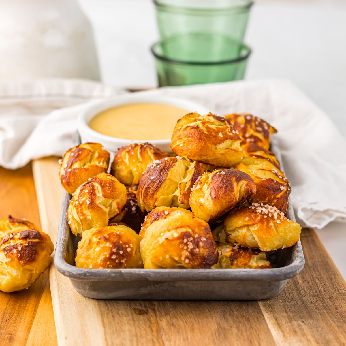 Easy Biscuit Pretzel Bites with Cheese Sauce on a tray sitting on table with a glass to the side 