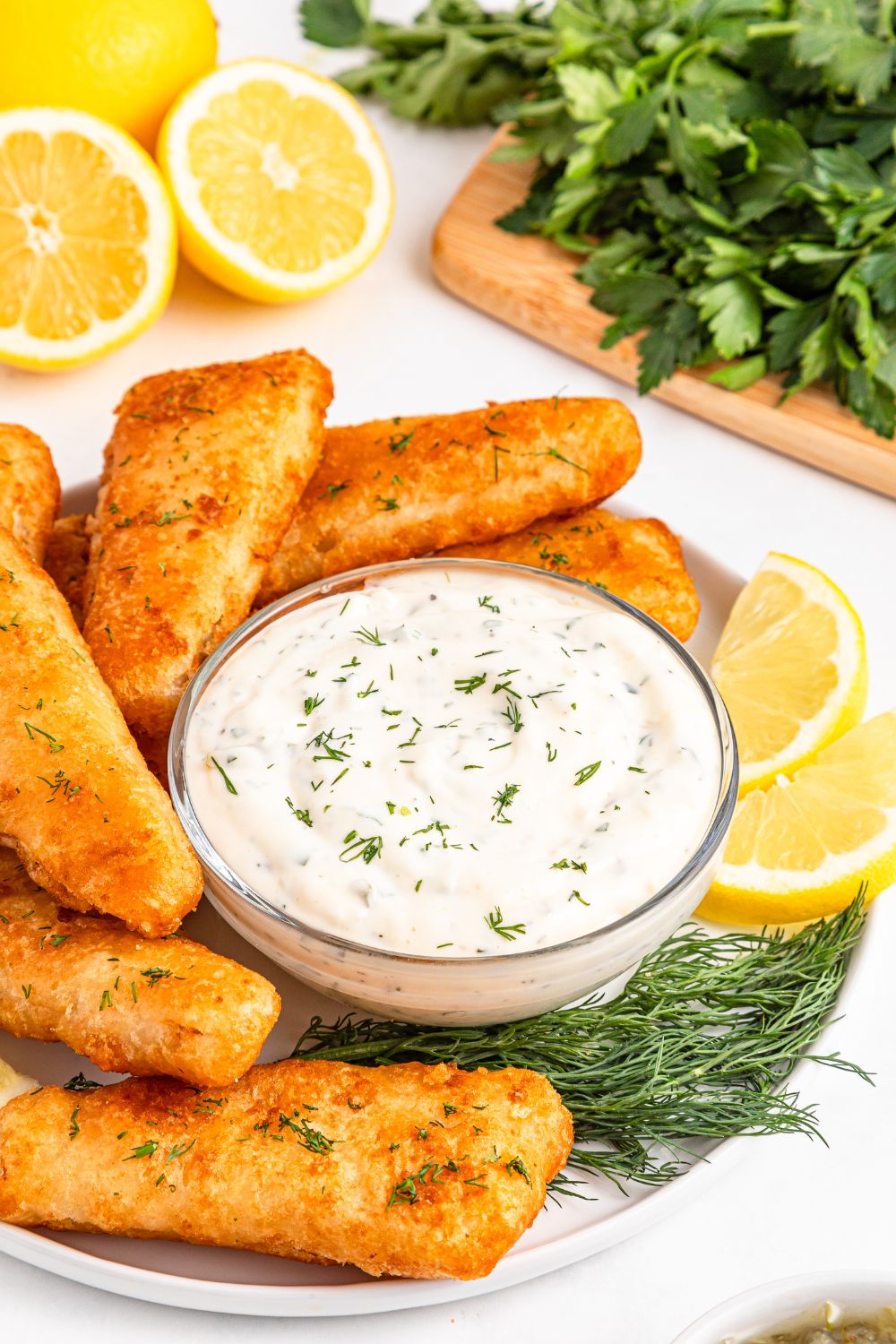 Easy Homemade Tarter Sauce in a glass jar with fish fillets on table with lemon wedges to side 