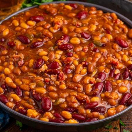 looking down to table with Crockpot Bourbon Brown Sugar Baked Beans in a serving bowl on a dark wood table