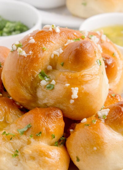 Homemade Garlic Knots piled out on a plate with butter, parsley and dipping sauces to side