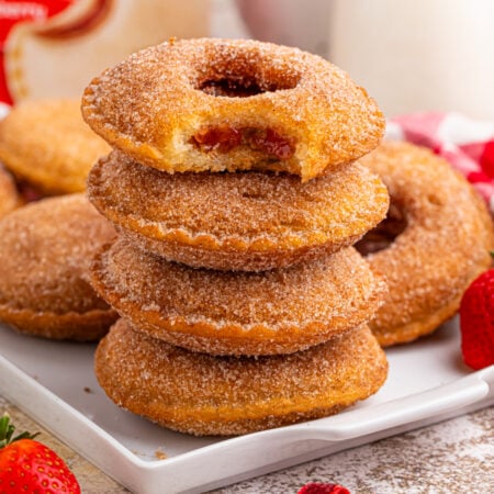 plate with Fried Strawberry Uncrustables that have been fried and rolled in sugar on plate with strawberries in front of plate
