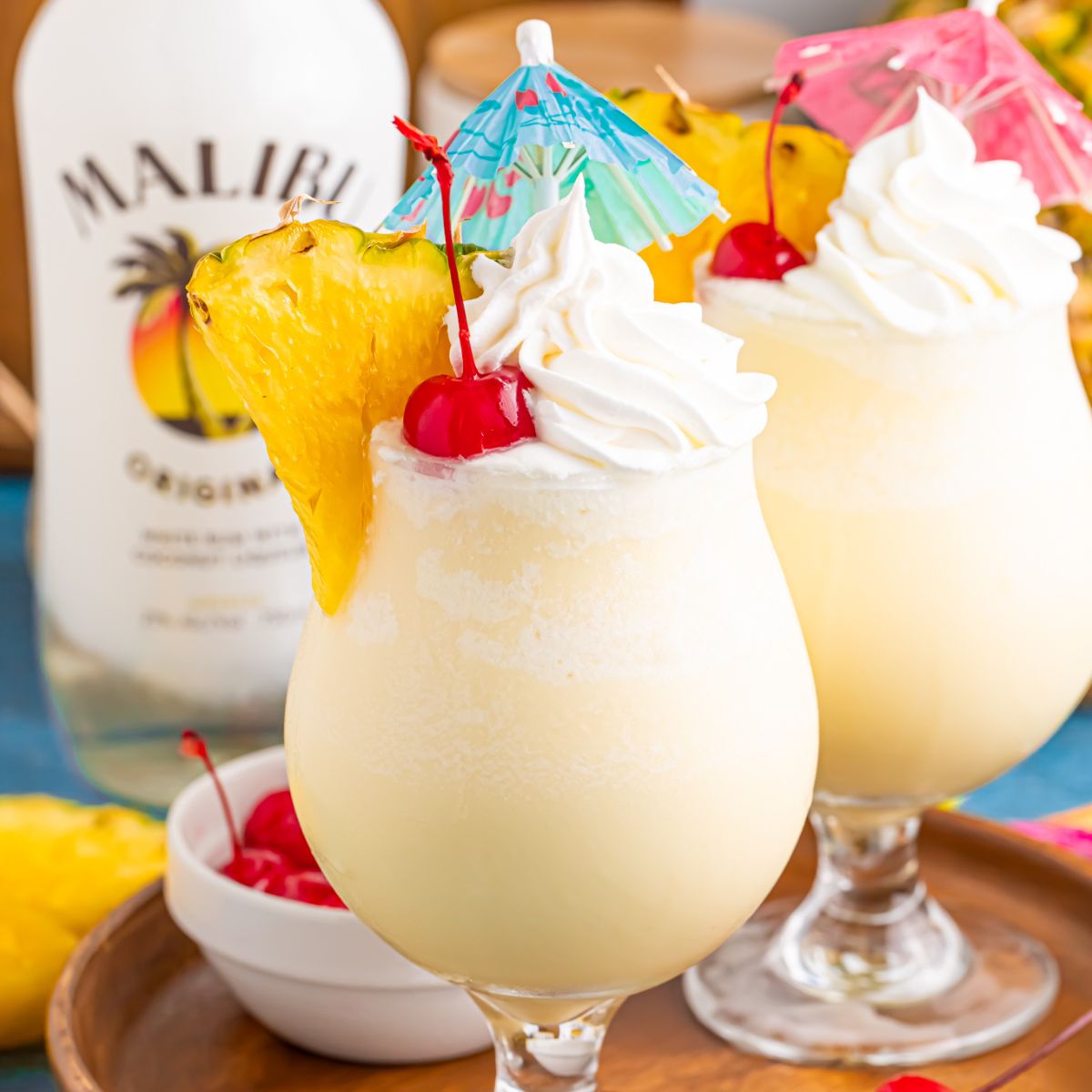 Frozen Malibu Piña Coladas in glasses with little umbrellas, pineapple slices and cherries