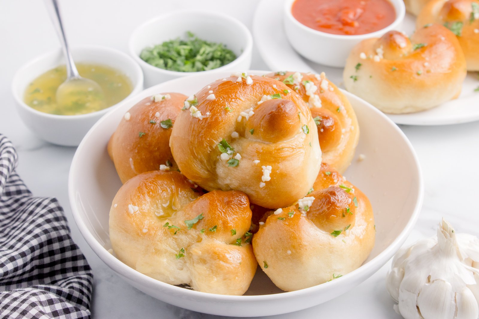 Homemade Garlic Knots on a plate with a bowl of marinara on side and garlic butter 