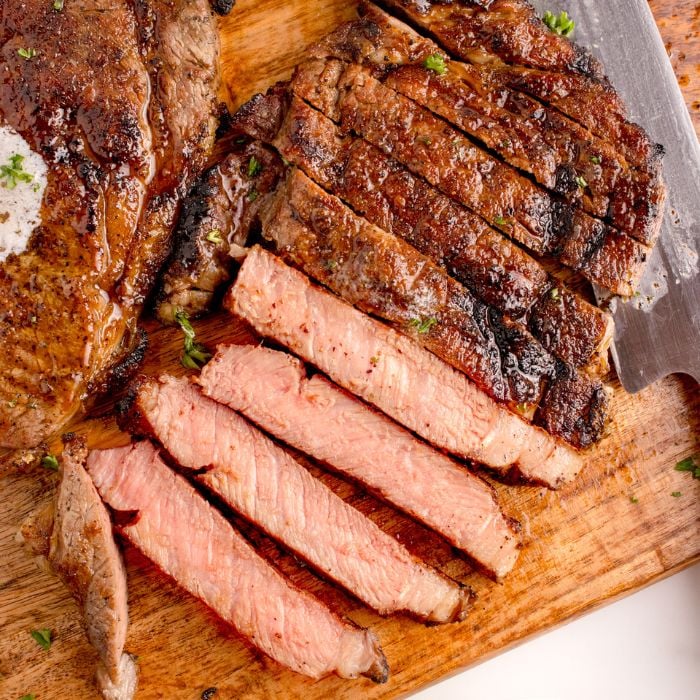 Grilled Ribeye Steak sliced on cutting board with a whole steak to side 