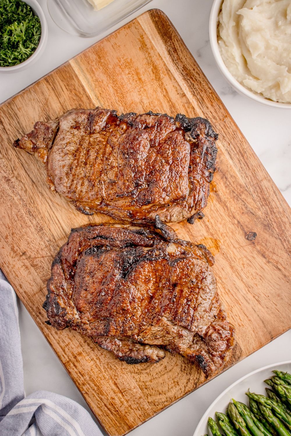 Grilled Ribeye Steaks on wooden cutting board sitting on table 