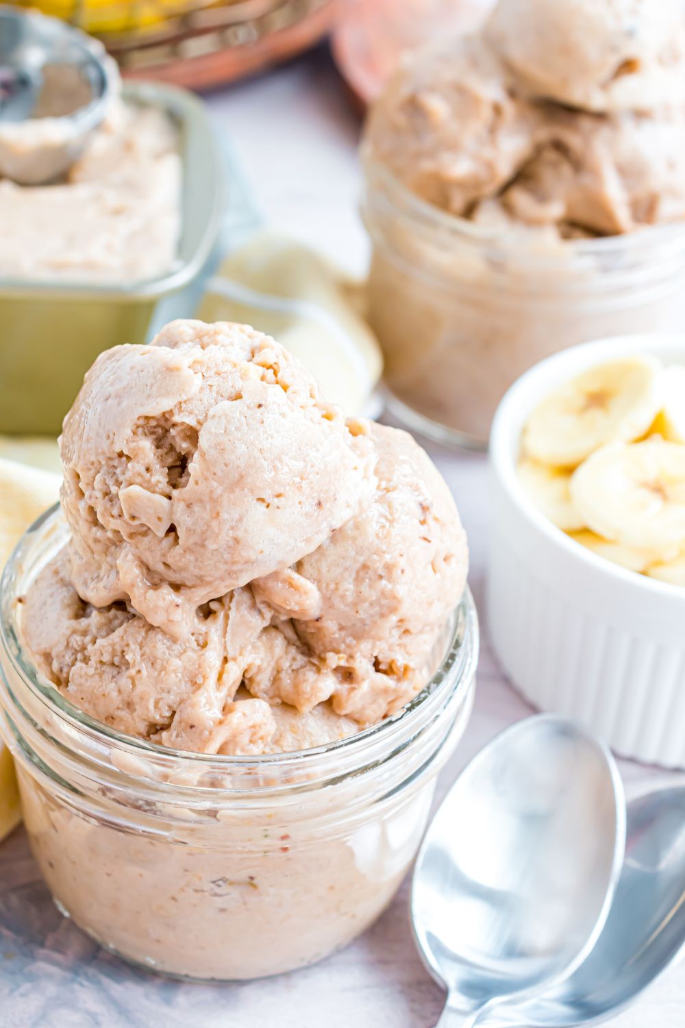 Banana Ice Cream in a glass bowl with fresh sliced bananas to side and spoons on table 