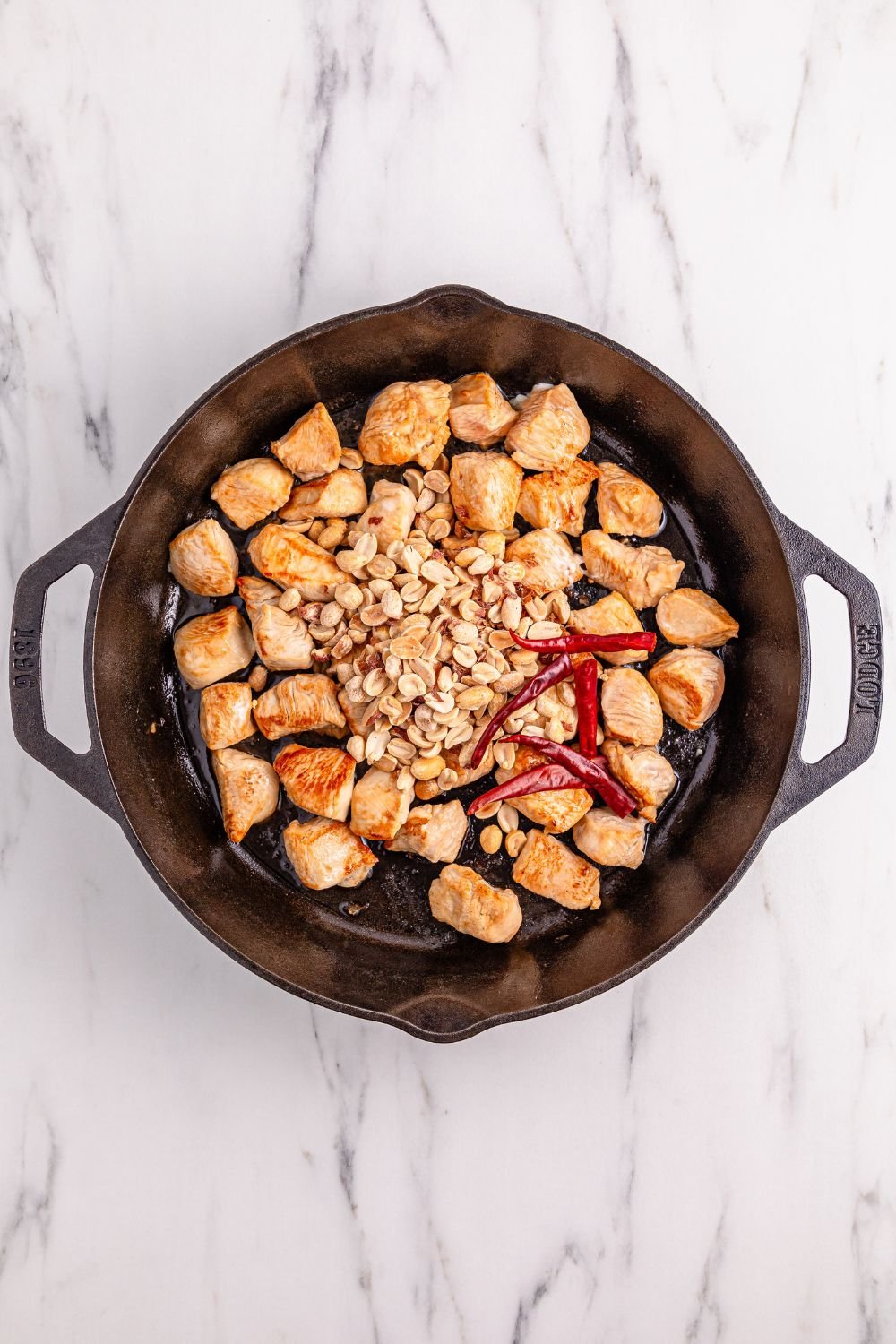 chicken in a cast iron skillet with ingredients in to make sauce for Better Than Takeout Kung Pao Chicken