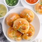 Homemade Garlic Knots piled out on a plate with butter, parsley and dipping sauces to side