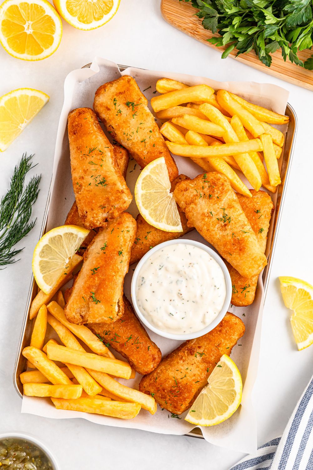 fish and chips on a platter with a bowl of homemade tartar sauce on tray with lemon wedges 