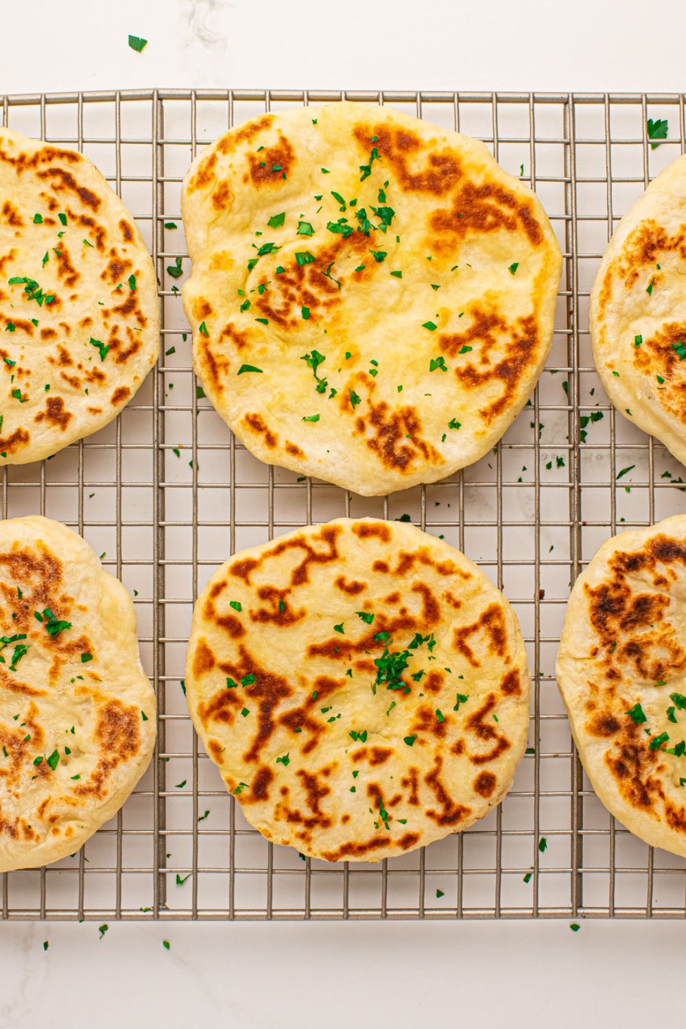 3 Ingredient Flatbreads spread out on cooling rack topped with butter and parsley flakes 