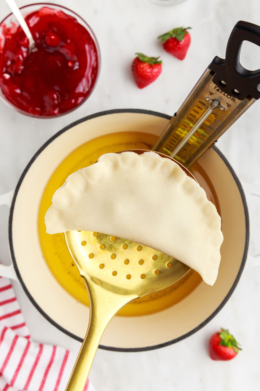 raw Deep Fried Strawberry Cheesecake Pie in a ladle with a pan of oil under it 