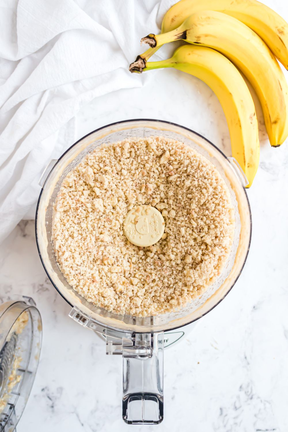 Banana Ice Cream being made in a food processor with a bundle of bananas to side 