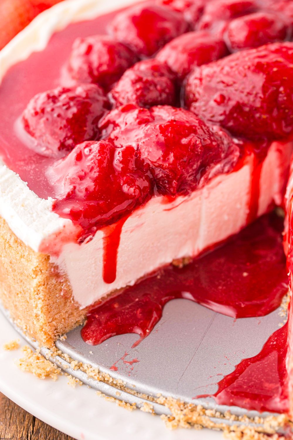 view of No Bake Strawberry Cheesecake on table with sauce dripping down on cheesecake 