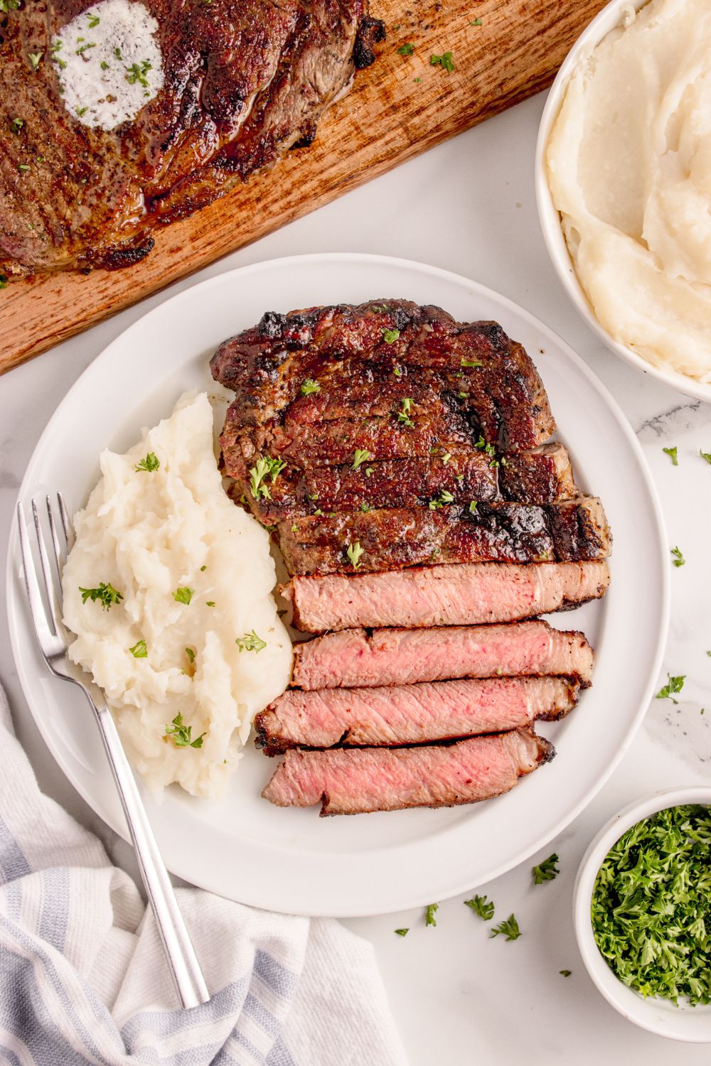 Grilled Ribeye Steak on plate with some mashed potatoes to side all garnished with parsley 
