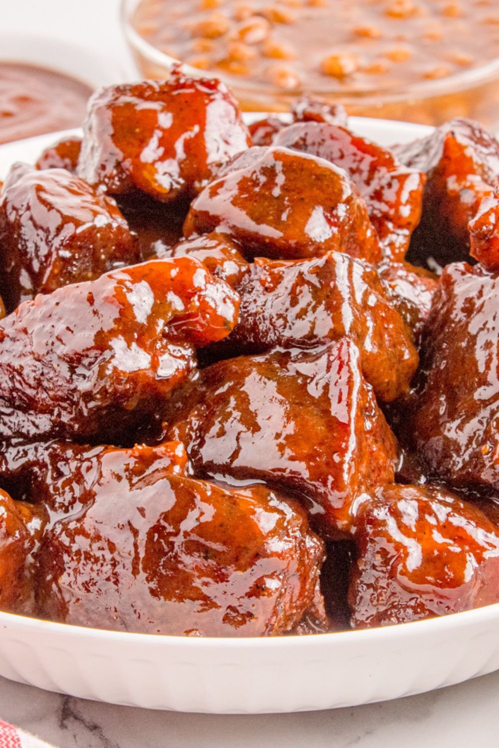 Chuck Roast Burnt Ends in a white bowl on a table with a bowl of beans to the side 