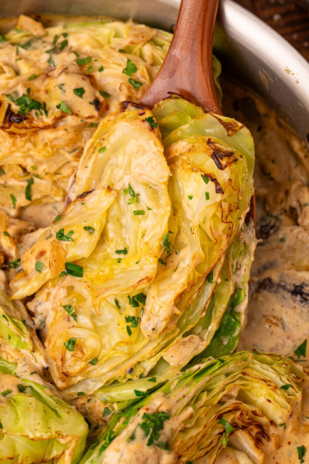 Creamy Garlic Parmesan Cabbage in a skillet being lifted out with a wooden spoon 