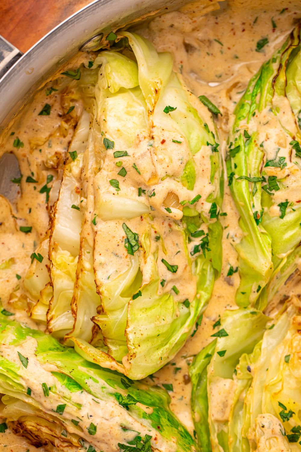 Creamy Garlic Parmesan Cabbage in a skillet on table with some parsley sprinkled over creamy sauce and the cabbage wedges 