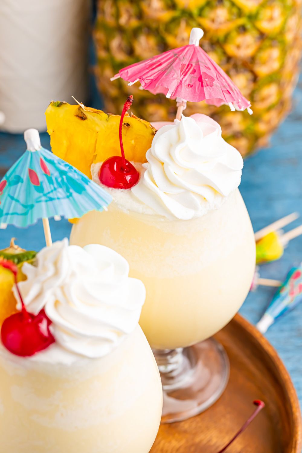 Frozen Malibu Piña Coladas on table with whipped cream, cherries, and umbrella, and more umbrella scattered on table 