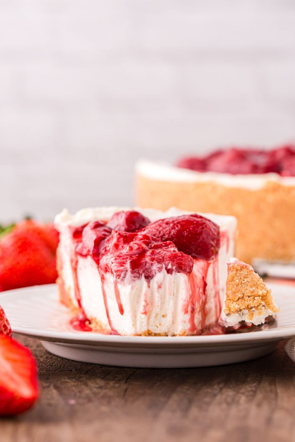 No Bake Strawberry Cheesecake on plate with a bite cut out and the rest of cheesecake behind it on table 