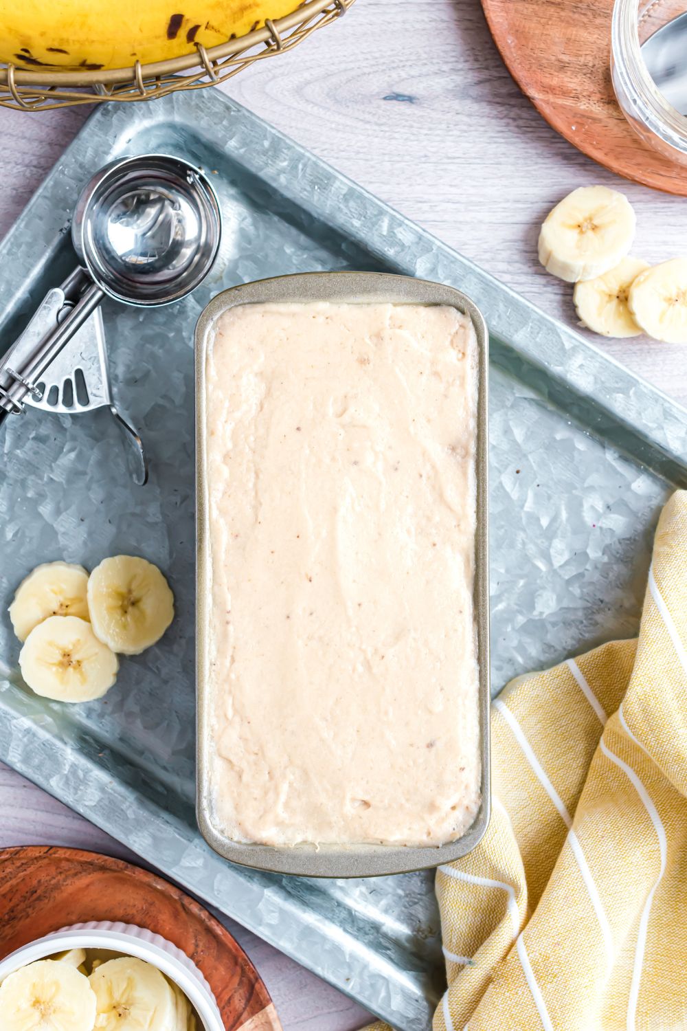Banana Ice Cream in a loaf pan with fresh bananas sliced to side and an ice cream scoop to side of pan 