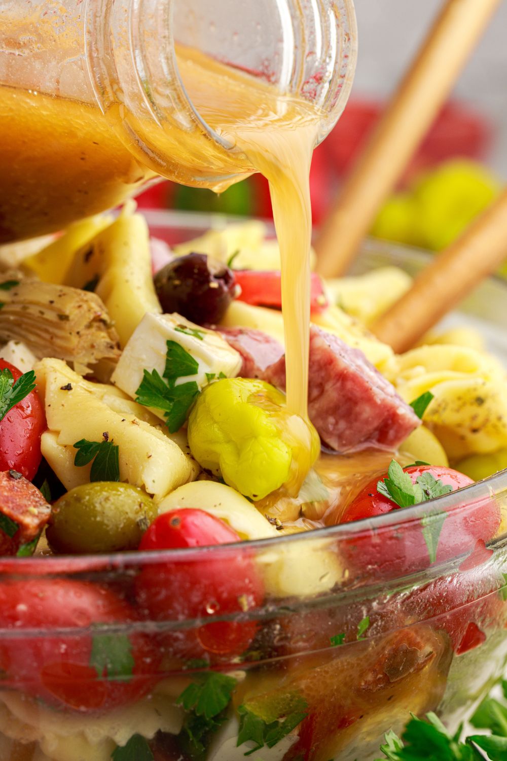 pouring dressing into a bowl of Antipasto Tortellini Pasta Salad