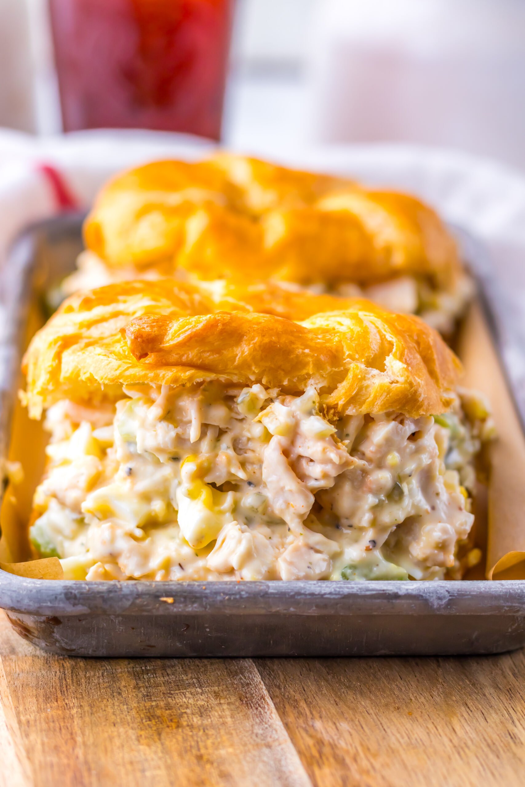 Close up shot of chicken salad on a white croissant on a tin tray.  
