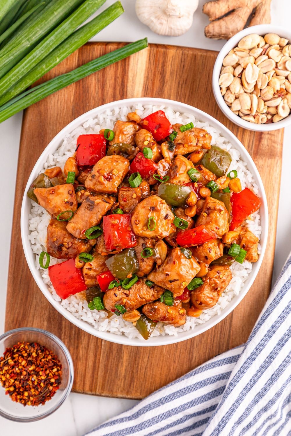 Better Than Takeout Kung Pao Chicken on a plate with nuts, green onions, ginger, garlic, red pepper flakes all around on table 