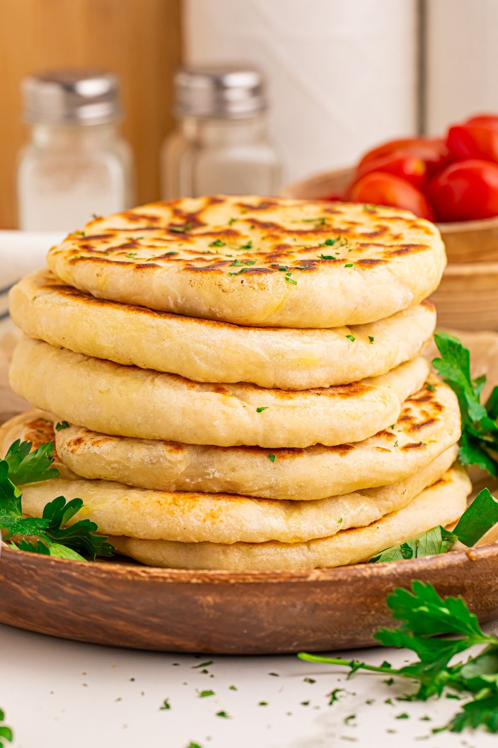 3 Ingredient Flatbread stacked on top of one another with parsley on side and bowl of tomatoes behind it 