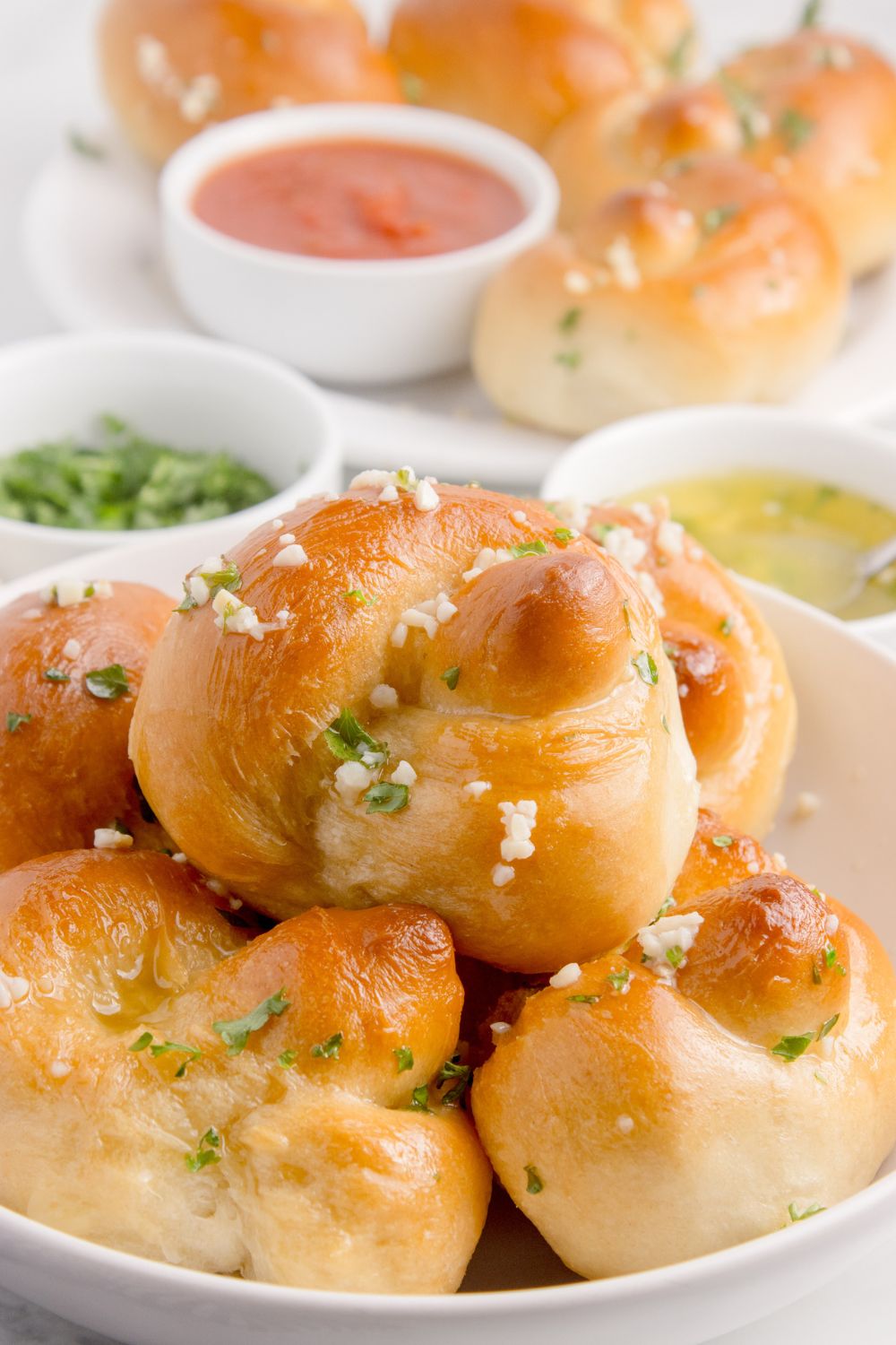 Homemade Garlic Knots in a bowl with garlic butter in a bowl, parsley and a bowl of marinara sauce 