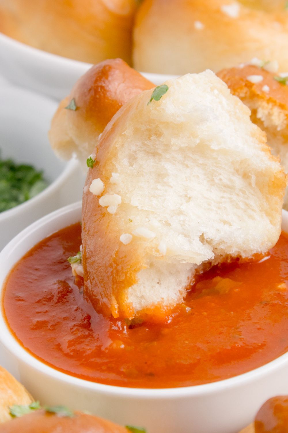 Homemade Garlic Knot being dipped into marinara sauce on table 