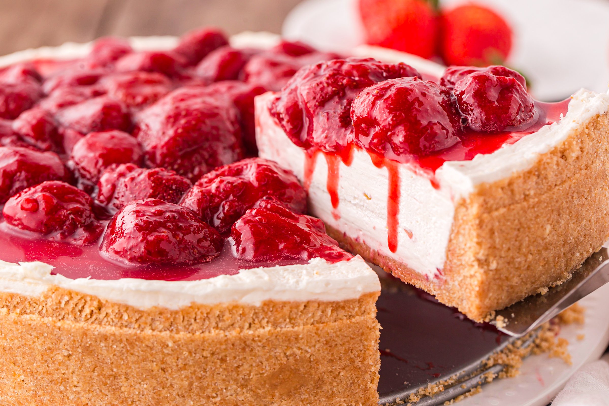 No Bake Strawberry Cheesecake being lifted out of pan with strawberries dripping down side of sliced cheesecake 