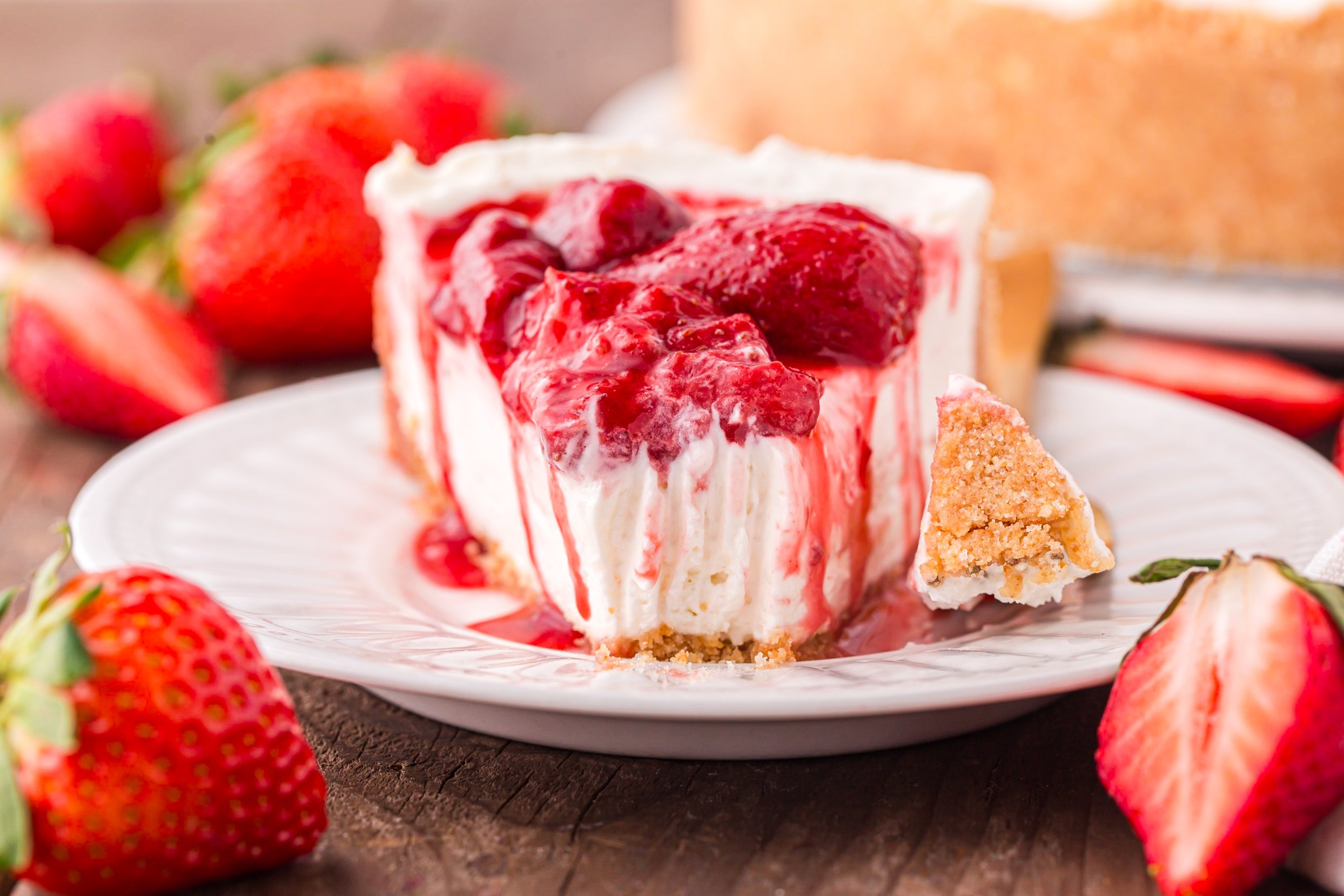 No Bake Strawberry Cheesecake  up close on a white plate, topped with juicy strawberries with a bite missing 