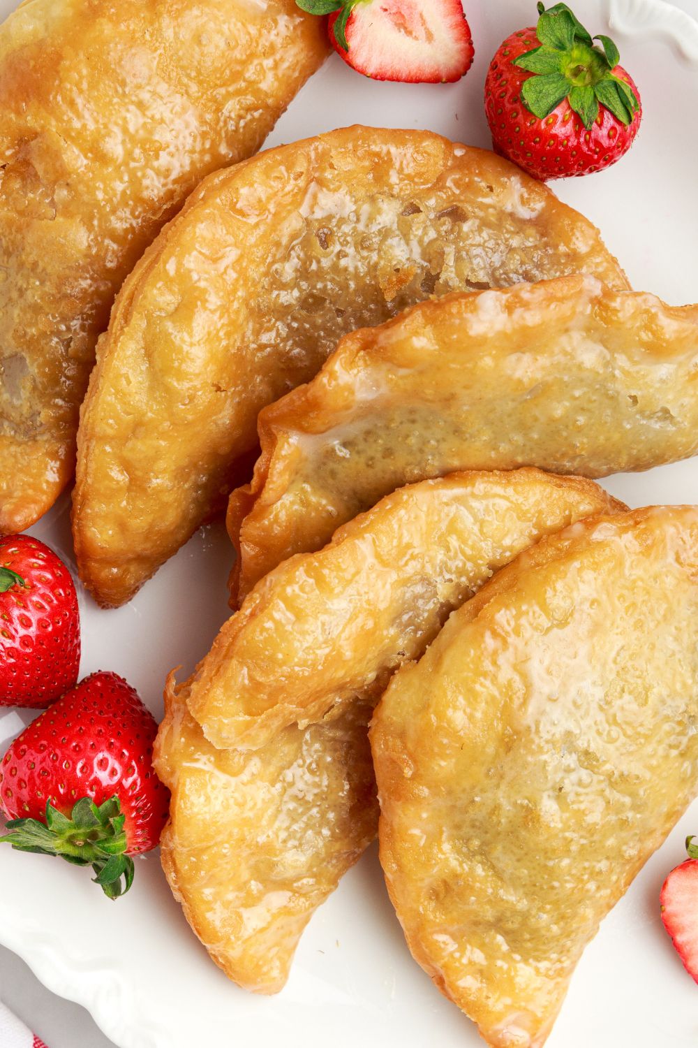 Deep Fried Strawberry Cheesecake Pies on a plate with some whole strawberries to side on plate 