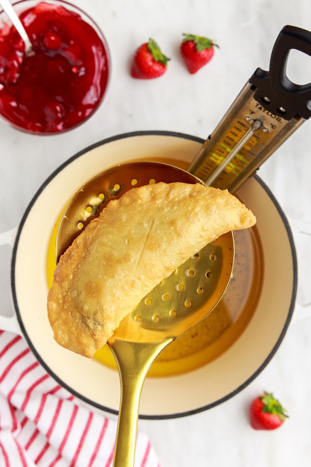  Deep Fried Strawberry Cheesecake Pie above a pot of oil  on a ladle 