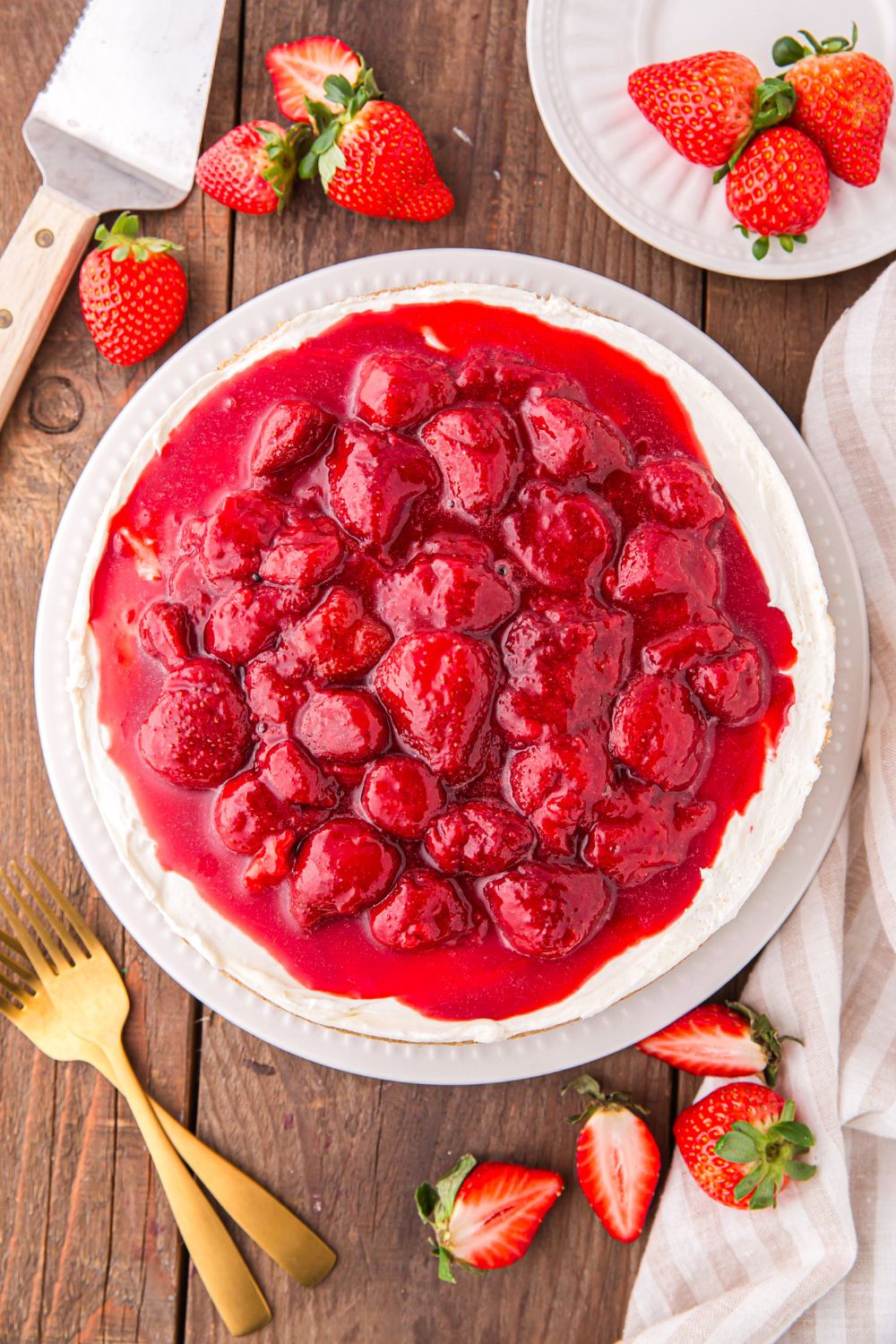 No Bake Strawberry Cheesecake sitting on table with fresh strawberries around it, forks, and plates 