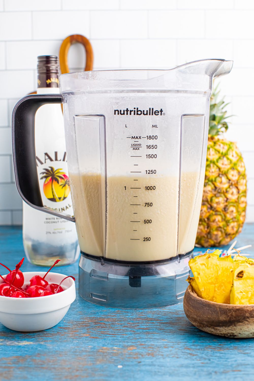 Frozen Malibu Piña Colada mixture in a blender sitting on table with pineapple, cherries, and pineapple 