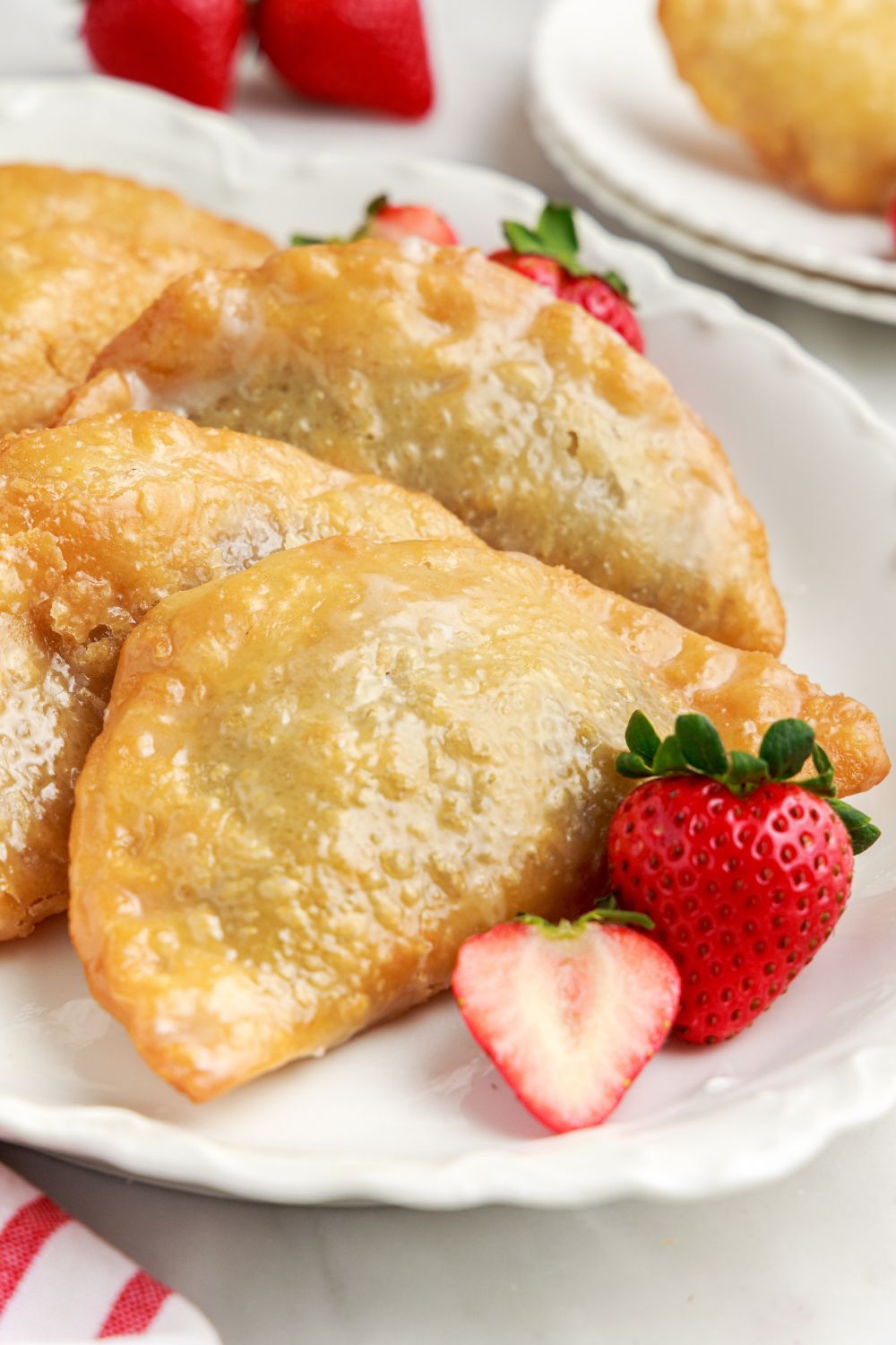 Deep Fried Strawberry Cheesecake Pies laid nicely on platter with some strawberries on plate 