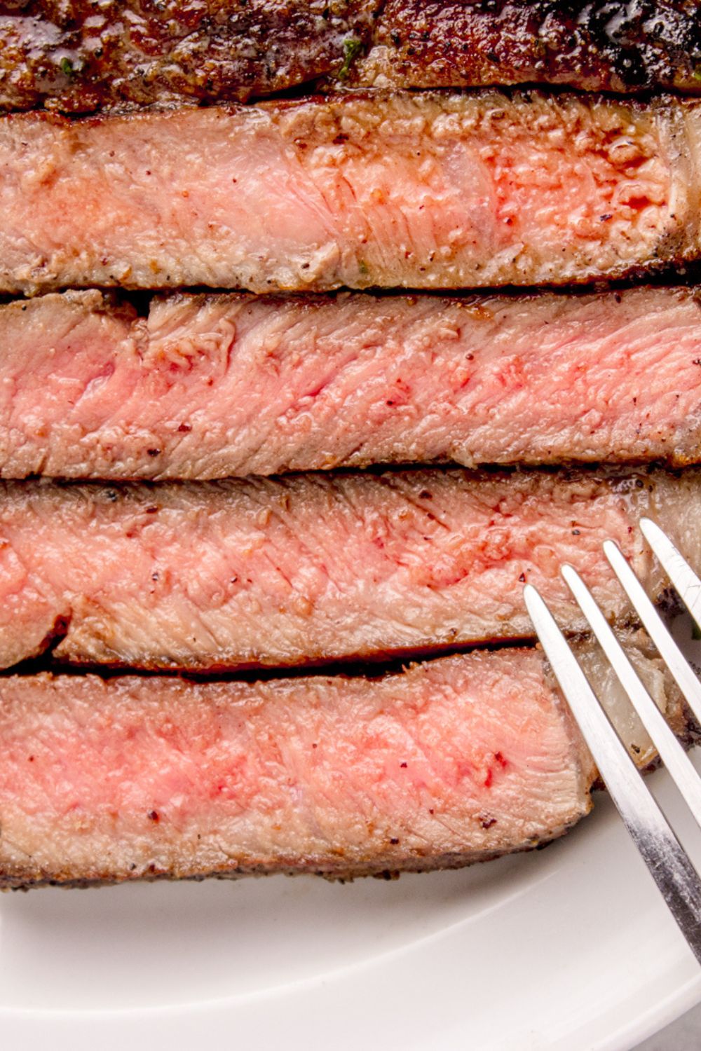 Grilled Ribeye Steak sliced into strips, with a close up of the redness and a fork to side 
