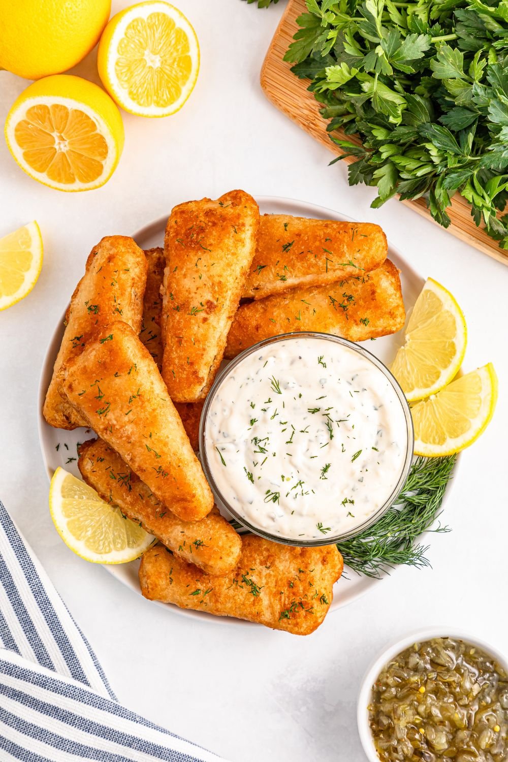 Easy Homemade Tarter Sauce in a bowl with fried fish fillets around it and lemons and dill to side of platter 