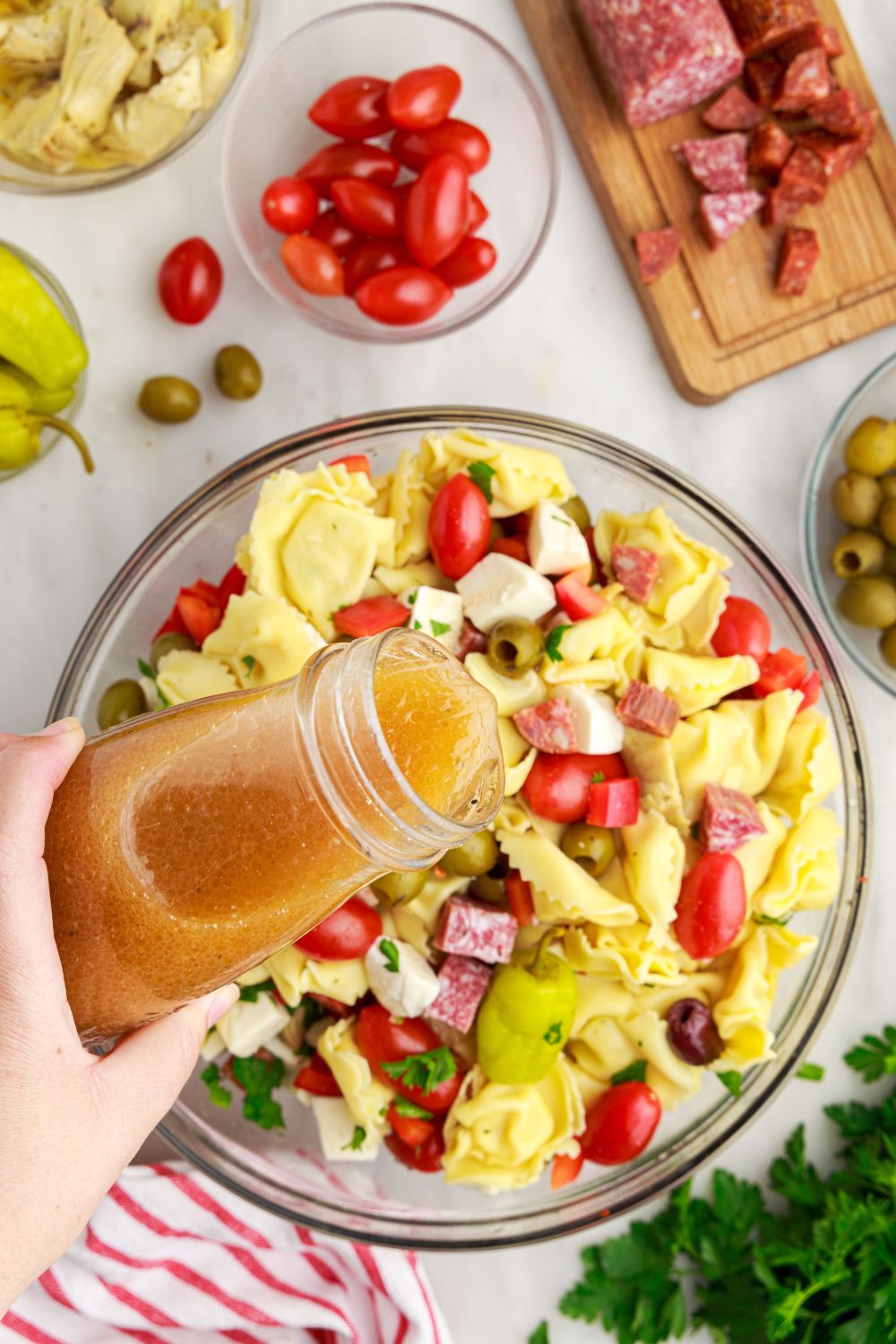 sauce pouring over Antipasto Tortellini Pasta Salad in a glass bowl