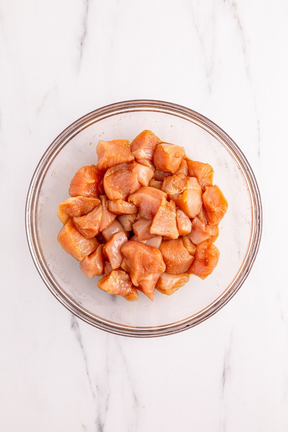 glass bowl with diced seasoned raw chicken 