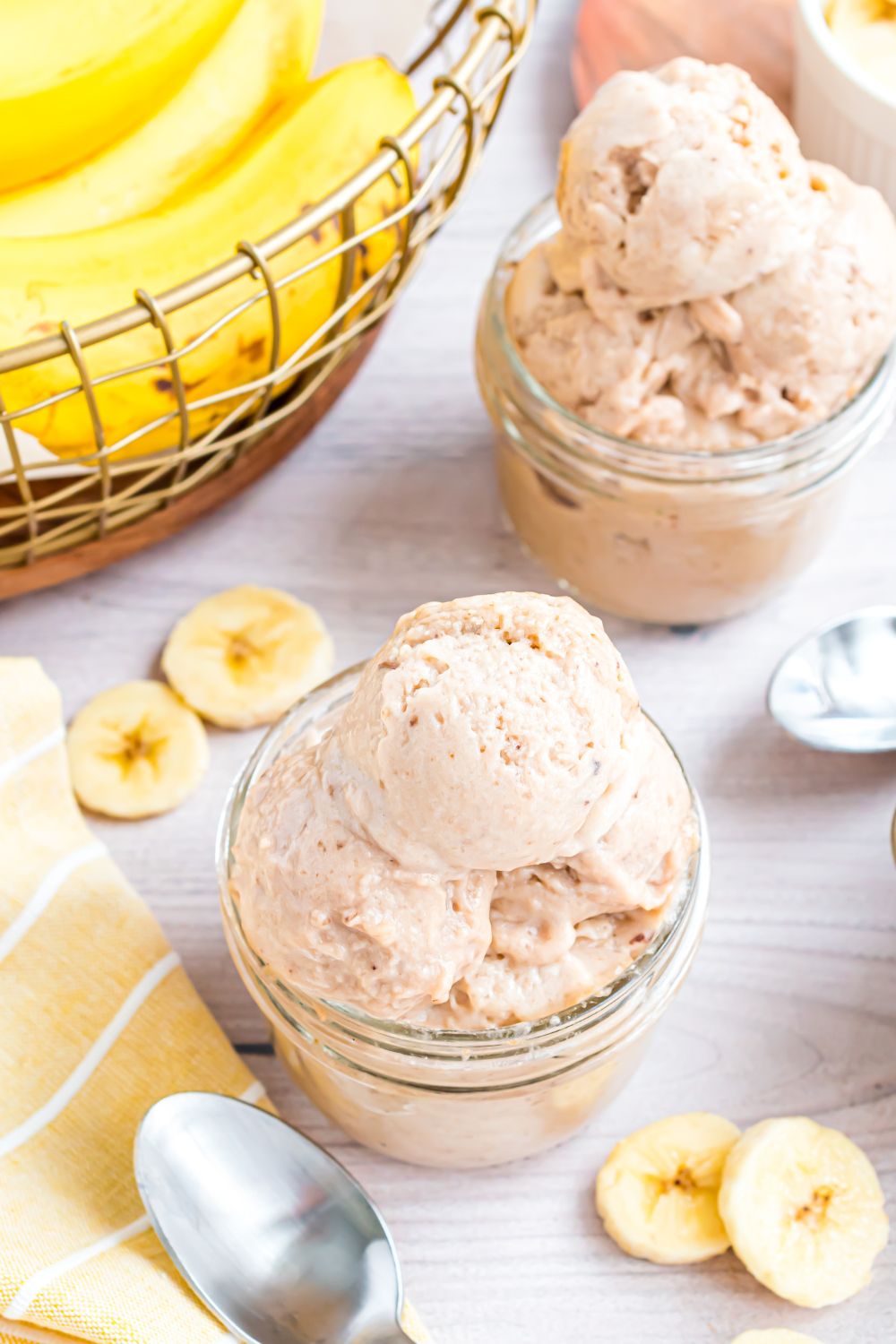 Banana Ice Cream in small bowls on table with a bundle of bananas to side and sliced bananas on table 