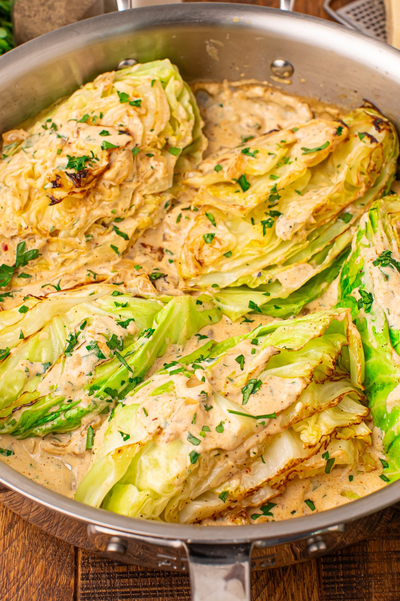 Creamy Garlic Parmesan Cabbage wedges in a skillet topped with cream sauce 