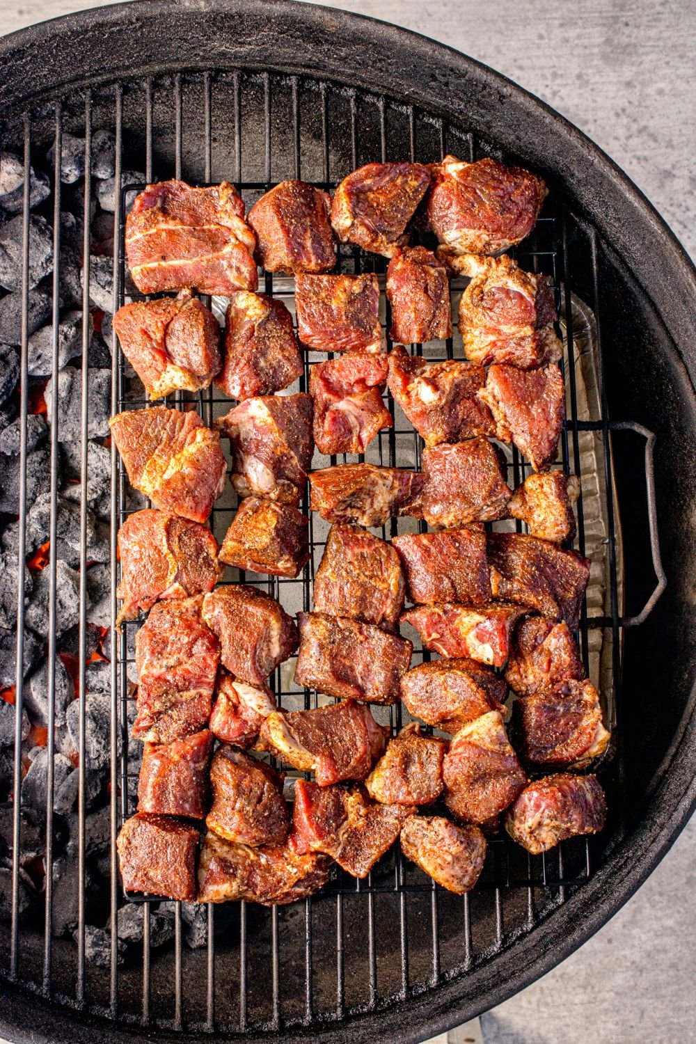 charcoal grill with pieces of steak spread out over it 